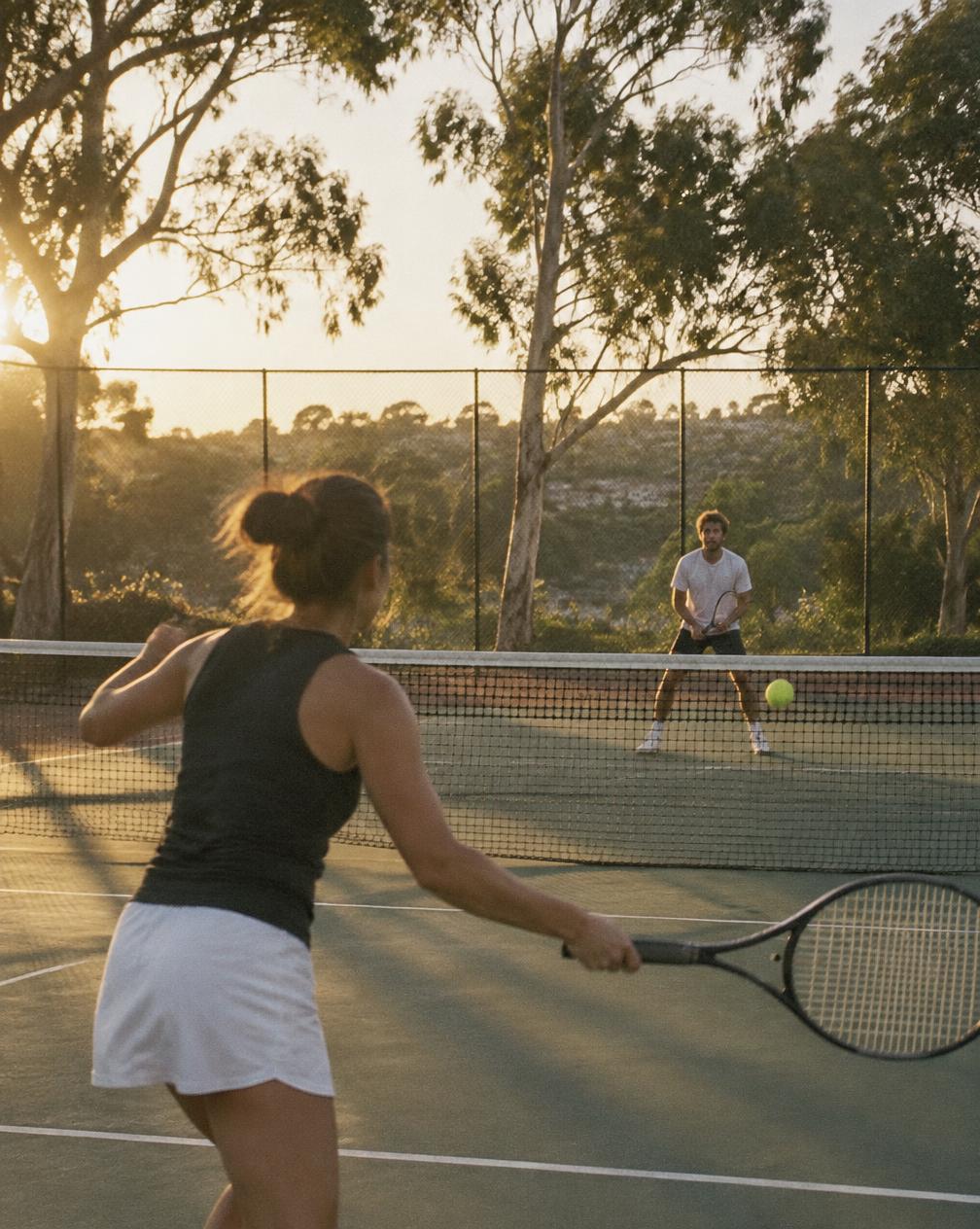 Two tennis players rallying on an outdoor court at golden hour